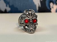 Front view of silver-tone skull ring showing red stone eyes and ornate detailing