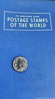 Front cover of blue Ambassador stamp album with coin placed on top