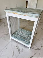 Three-quarter view showing teal plank top, white frame, lower teal shelf