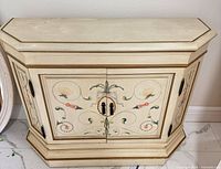Front view of painted wood console cabinet showing floral motifs, double doors, hardware