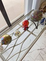 All four glass orbs lined left to right on table with iron stand supporting largest orb