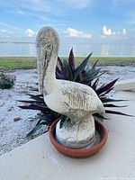 Front left view of weathered concrete pelican statue on saucer