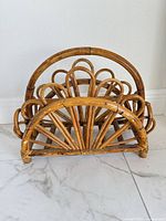 Front angled view of vintage rattan magazine rack showing arched form and honey finish