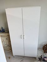 Front view of closed white two-door cabinet showing handles and full height