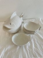 Covered fish tureen alongside stack of six fish plates