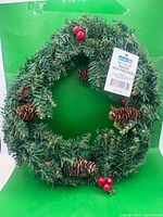 Full view of evergreen wreath showing pinecones, red berries, tag attached