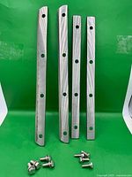 Four straight metal blades and eight bolts displayed on green backdrop