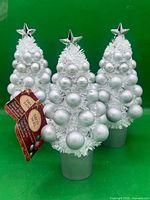 Three white tinsel tabletop Christmas trees with silver ornaments and star toppers