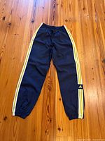 Full front view of navy adidas track pants with yellow stripes