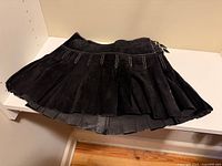 Front view of black faux suede pleated mini skirt on shelf showing overall design and pleats
