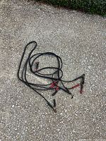 Coiled black jumper cables with red and black clamps on gravel surface