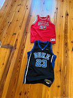Chicago Bulls red jersey and Duke black jersey full view on wood floor
