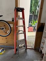 Red fiberglass step ladder and silver aluminum step stool leaning against garage wall