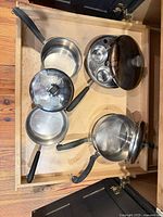 Drawer view of three saucepans, lids, nested cups