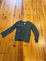 Sweater front view laid flat showing cable knit pattern and overall condition