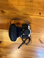 Top view of Pentax K1000 camera with lens cap and case on wooden surface