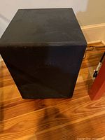Front angled view of black subwoofer showing cloth grille and scuffed cabinet