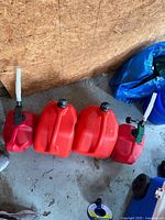 Four red plastic fuel cans arranged side-by-side showing caps and spouts