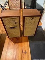 Front view of both wood veneer speakers with worn beige grilles and logo badges