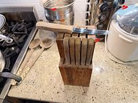Front view of wooden knife block with six serrated knives, one partially removed