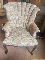 Front view of armchair showing floral tapestry upholstery, channel back, wood cabriole legs
