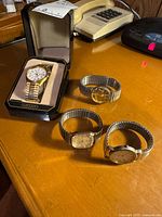 Seiko watch in box and three additional gold-tone watches on table