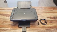 Top view of Canon MG3029 printer scanner with paper tray open and power cable alongside