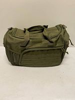 Front view of olive drab tactical duffle showing MOLLE webbing, mesh pocket, carry handles