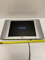 Front view of Legend LEC1524 LCD TV powered on displaying logo, tape measure shows width