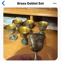 Six small brass goblets displayed on wooden surface