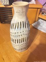 Front view of cream ceramic vase showing textured dash and dot pattern and Artisan de Luxe label