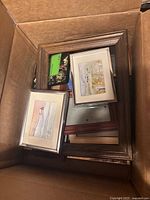 Box containing assorted wood and metal picture frames, two matted artwork inserts visible