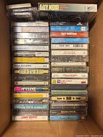 Box containing stacked pre-recorded cassette tapes showing various titles and the portable cassette player partially visible