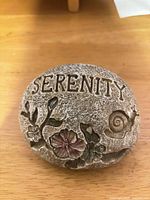 Front of resin garden stone showing SERENITY text, flower and snail relief