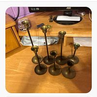Seven brass candlesticks on wooden desk, varying heights