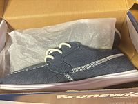 Side view of shoe in box showing denim upper, stitching, laces