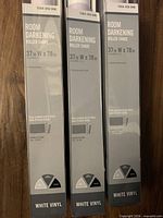 Front view of three boxed white vinyl roller shades showing product name and dimensions