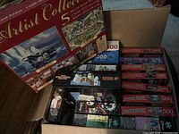 Open carton showing Artist Collection 5-puzzle box and multiple Puzzlebug 500-piece boxes