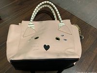 Front of light pink Betsey Johnson handbag showing cat face design and striped handles