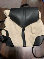 Front view showing beige canvas body and black faux leather flap and bottom corners