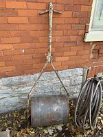 Full view of metal lawn roller leaning against brick wall