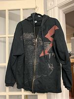 Front view of black zip hoodie with creature and lightning graphic