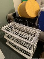 White multi-tier shoe rack in front of black laundry basket holding yellow and maroon buckets