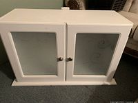 Front view of white two-door cabinet with frosted glass panels and knobs