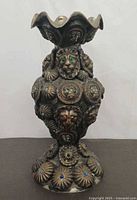 Front view of cast metal vase showing lion head relief and cabochon stones
