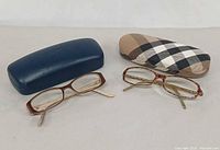 Two eyeglass frames with respective cases on neutral background