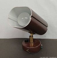 Front view showing cylindrical brown metal shade with white interior and bulb fitted, mounted on round base