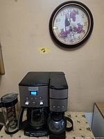 Front view of coffee maker with wall clock in background
