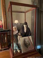 Overall view showing wood and glass curio cabinet containing three dolls and a Marilyn Monroe print