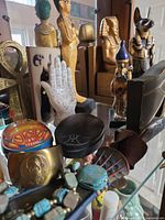 Overall view of figurines, ankh, hamsa plaque, scarab boxes and beads on glass shelf